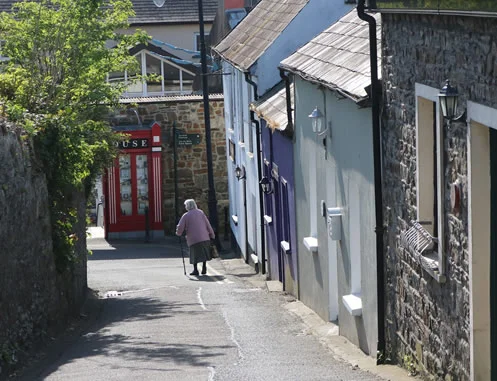 Elderly lady walking through a typical urban Irish back street. Aqua Control water purification for communities and group water schemes.