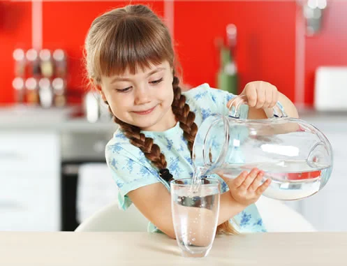 Young girl pours safe clean drinking water from Glass jug to glass beaker